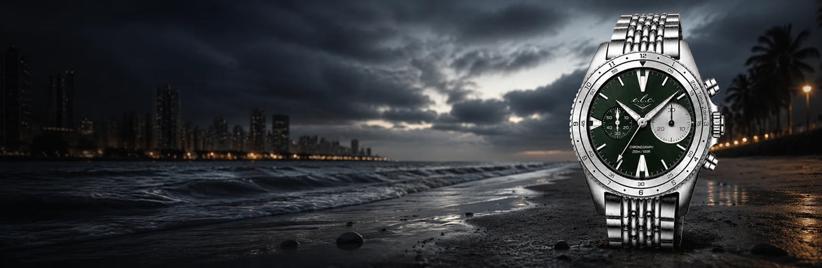 E.L.C. Riviera Signature Silver Green chronograph watch displayed on a dark beach at night with a city skyline in the background.